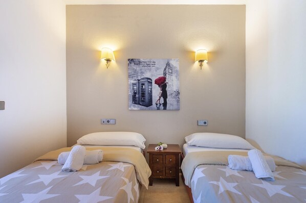 Habitación de hotel con dos camas, cada una con una colcha estampada con motivos de estrellas y almohadas blancas. Dos lámparas de pared a ambos lados de un cuadro enmarcado.