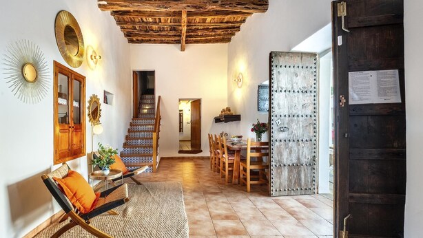 A hallway with a wooden staircase, a dining area with wooden chairs, a large mirror, and a rustic door.