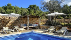 A pool area with lounge chairs and umbrellas, surrounded by stone walls and trees.