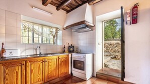 A kitchen with wooden cabinets, a stove, and a window overlooking a stone wall.