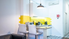 Une cuisine moderne avec des carreaux jaunes, un coin bar avec deux chaises blanches et un canapé en cuir noir.
