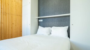 Un lit avec du linge de lit blanc, une tête de lit grise à texture et un mur composé de lattes de bois.