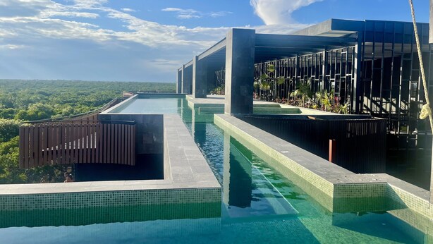 A modern infinity pool with a clear view of the landscape, a contemporary building with large windows, and a wooden deck area. - OVA CANCUN Y TULUM (Tulum)
