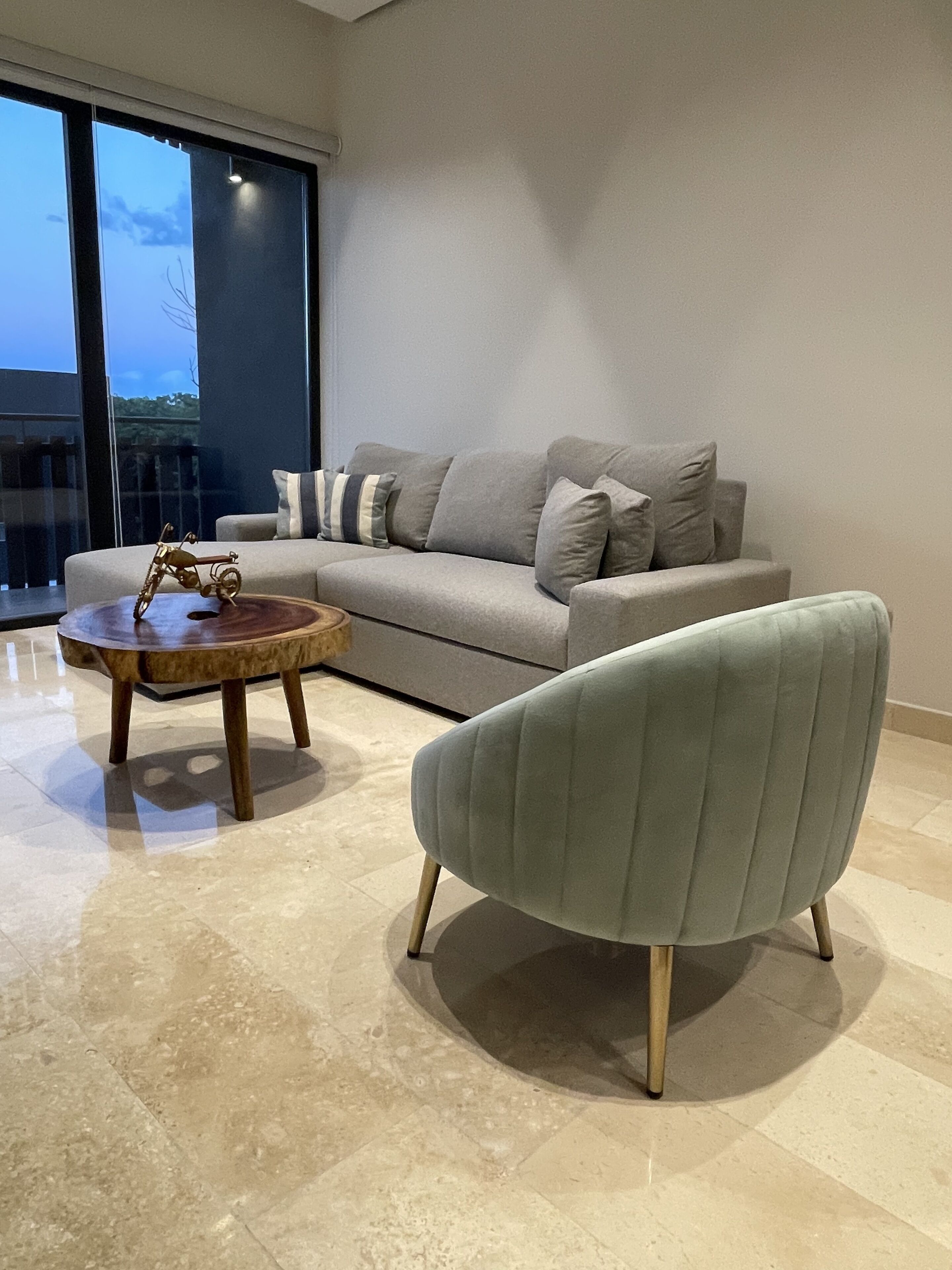 Un salón moderno con un sofá gris, una mesa de centro redonda de madera y un sillón verde claro.
