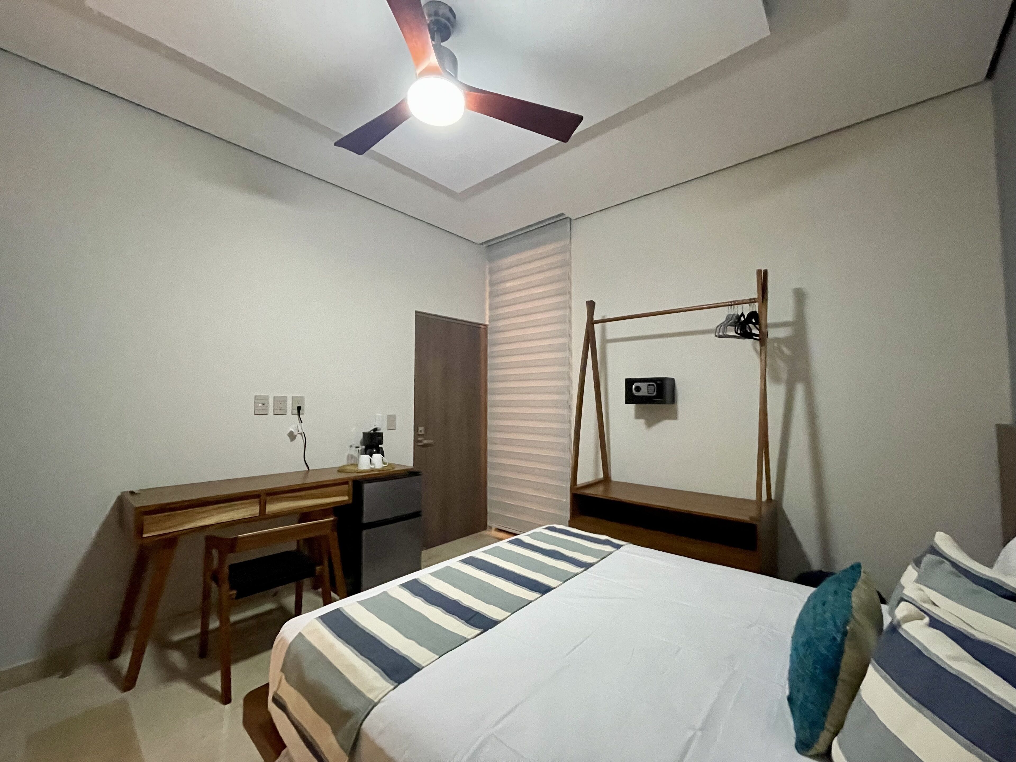 A bedroom with a bed, a desk, a chair, a wardrobe, and a ceiling fan.