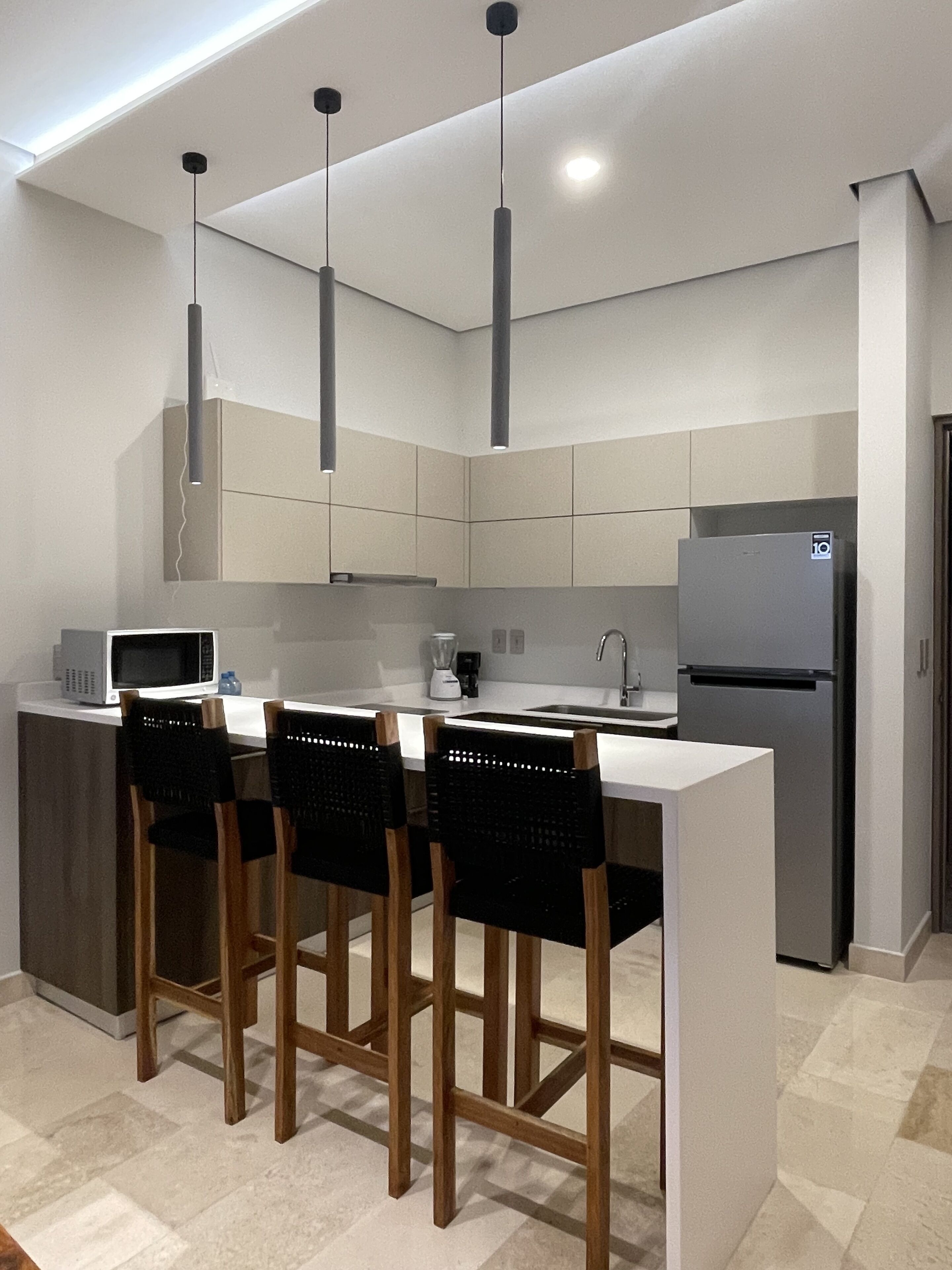 Una cocina moderna con una isla central, taburetes de bar, un refrigerador e iluminación colgante.