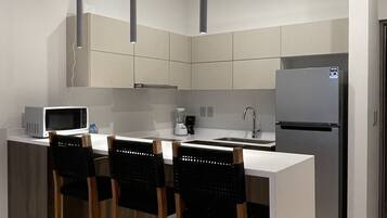 Una cocina moderna con una isla central, taburetes de bar, un refrigerador e iluminación colgante.