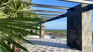 A modern outdoor patio with a checkered tile floor, metal beams, and a view of the ocean. - OVA CANCUN Y TULUM (Tulum)