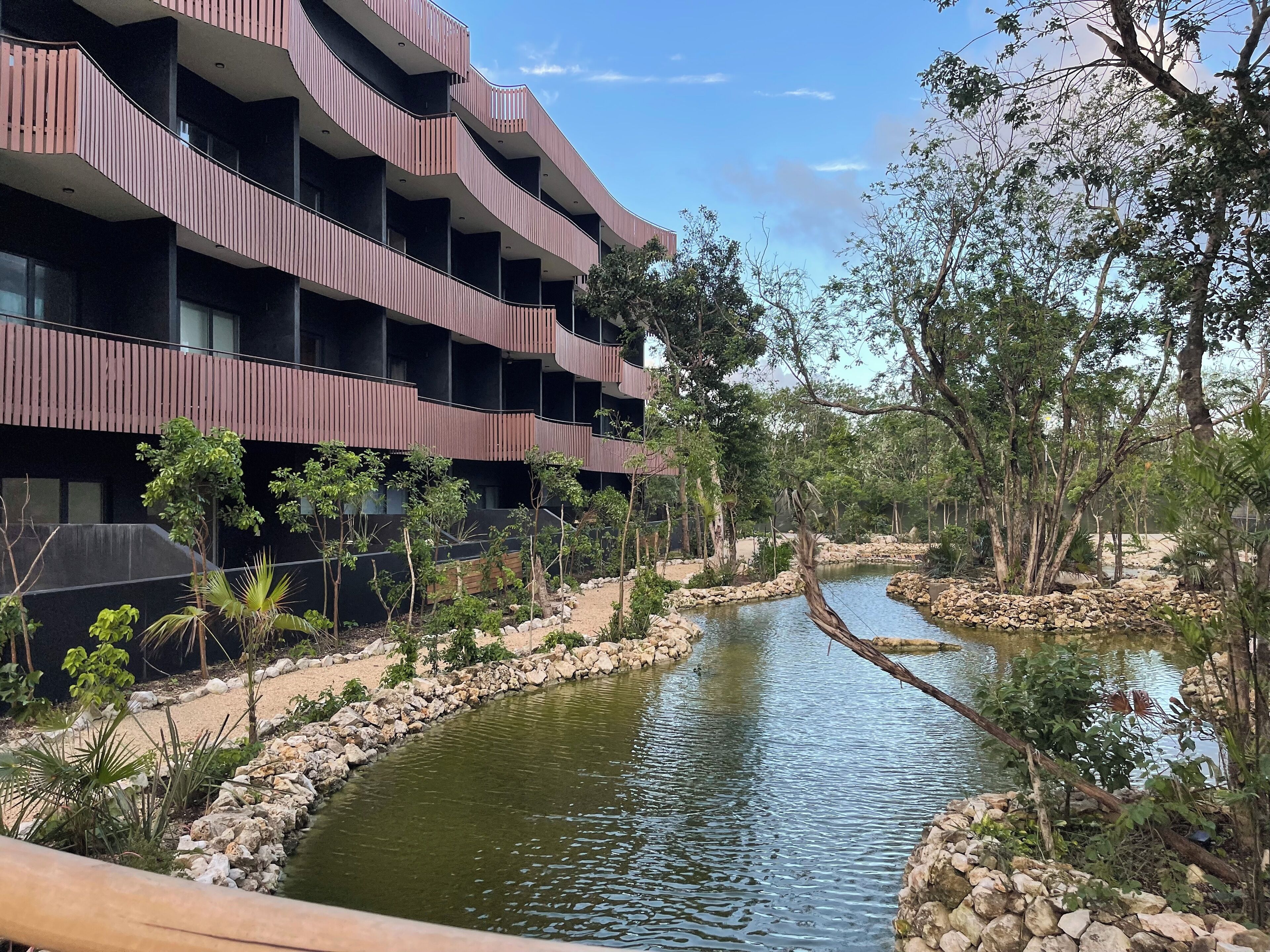 Un bâtiment moderne doté de nombreux balcons donnant sur un espace paysager agrémenté d’un élément aquatique.