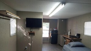 A compact room with a bed, a kitchenette, a television, and a door leading to another room.