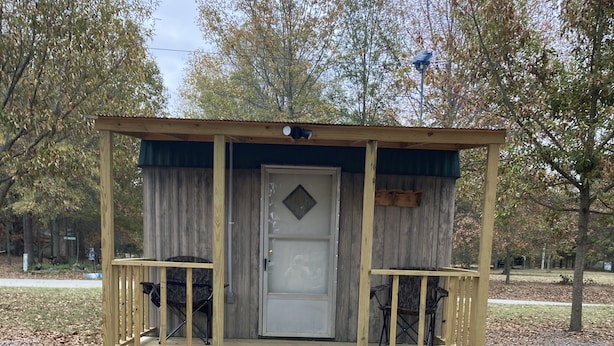 A wooden cabin with a porch, a door, and a small set of steps leading up to it.