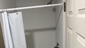 A small, enclosed shower area with a white shower curtain, a handheld showerhead, and a door with a handle.