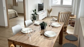 A modern dining area with a wooden table set for four, a television on a white cabinet, and a view of a snowy landscape through the window.