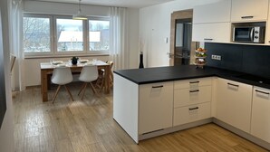 A modern kitchen with white cabinets, a black countertop, and a dining area with a wooden table and chairs.