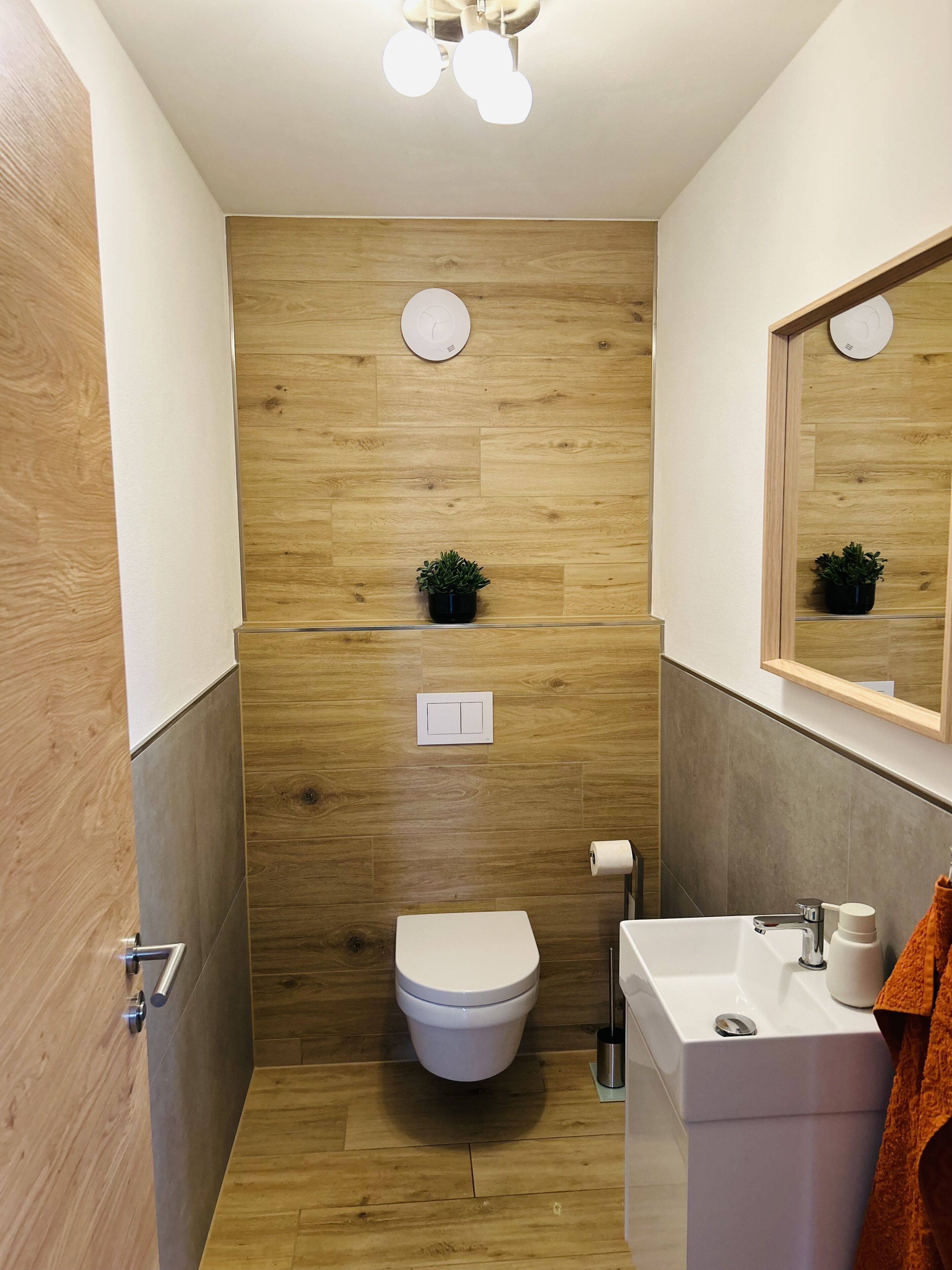 Ein modernes Badezimmer mit Holzwand, Toilette, Waschbecken und Spiegel.