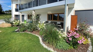 A modern two-story house with a balcony, surrounded by a well-maintained garden with various plants and flowers.