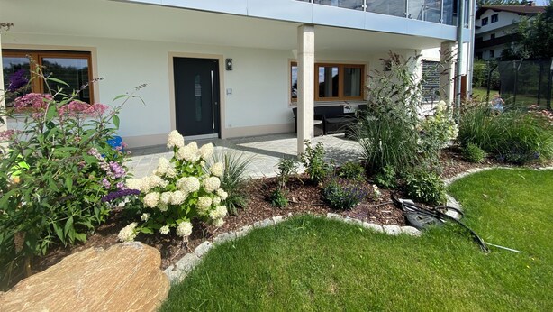 A modern two-story house with a balcony, a front door, and a small patio area with outdoor furniture.