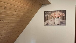 A room with a wooden sloped ceiling and a white wall. There is a poster of pink roses on the wall. - Apartment Beny (Bad Bellingen)