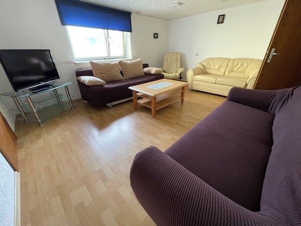 A living room with a sofa, a chair, a coffee table, and a TV on a glass stand. - Apartment Beny (Bad Bellingen)