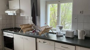 A compact kitchen with white cabinets, a built-in oven, a dishwasher, and a window providing natural light. - Apartment Beny (Bad Bellingen)