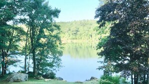 Une zone herbeuse avec quatre fauteuils Adirondack disposés face à un lac paisible, entouré d’arbres.