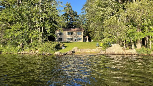 Une maison entourée d’arbres et bordée par un plan d’eau.