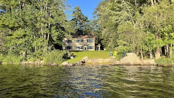 Une maison entourée d’arbres et bordée par un plan d’eau.