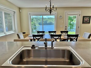 A kitchen with a stainless steel sink, a chandelier, and a dining area with a view of a lake. - Winter Lakefront Escape, Ice Fishing & Skiing (Turner)
