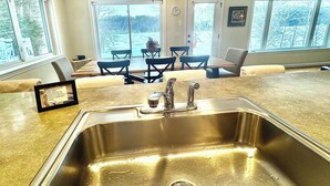 Une cuisine dotée d’un évier en acier inoxydable, d’un lustre et d’un coin repas avec des chaises et une table.