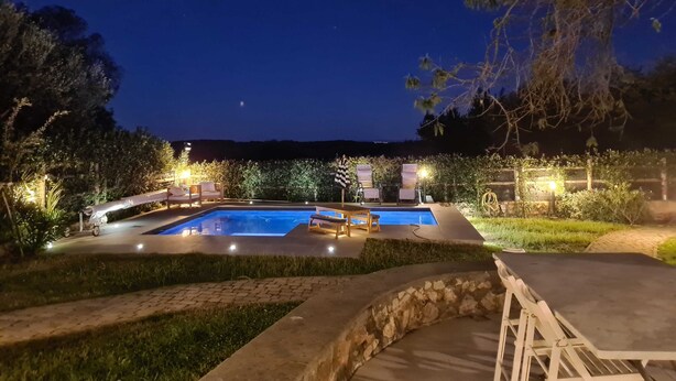 A nighttime view of a swimming pool area with a stone bench, lounge chairs, and well-lit pathways. - Lovely Portion of Villa in Ansedonia with swimming pool, 10' walk from Feniglia (Ansedonia)