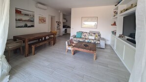 A spacious living area with a wooden dining table, a sofa, and a TV. - Lovely Portion of Villa in Ansedonia with swimming pool, 10' walk from Feniglia (Ansedonia)