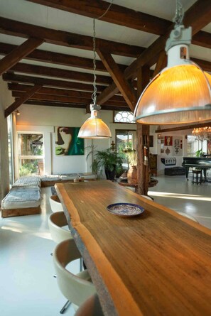 Een ruime kamer met een lange houten tafel, hangende吊り下げ照明 en een piano.