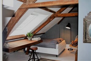 Slaapkamer in loftstijl met schuine wanden, een bed, bureau, stoel en hanglamp.