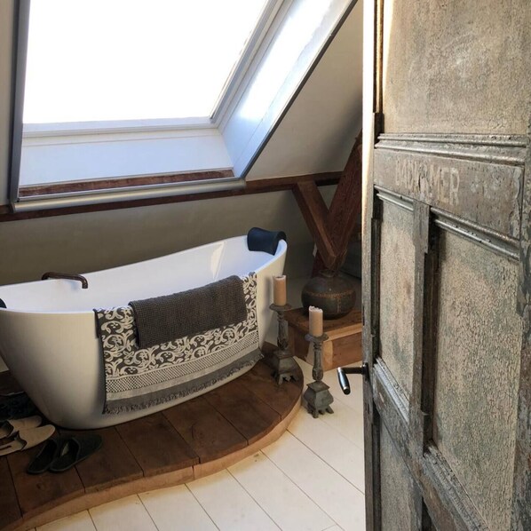 Une chambre mansardée avec un plafond haut, une fenêtre de toit, une baignoire, une cheminée et un plancher en bois.