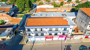 A hotel with a red and white facade, multiple balconies, and a parking lot in front. - Pinheiro Flat Hotel (Ibiapina)