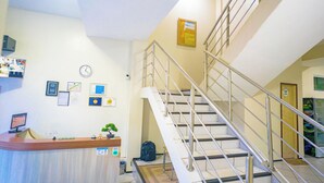 A reception area with a desk, computer, and various certificates on the wall. A staircase with metal railings leads to another floor. - Pinheiro Flat Hotel (Ibiapina)