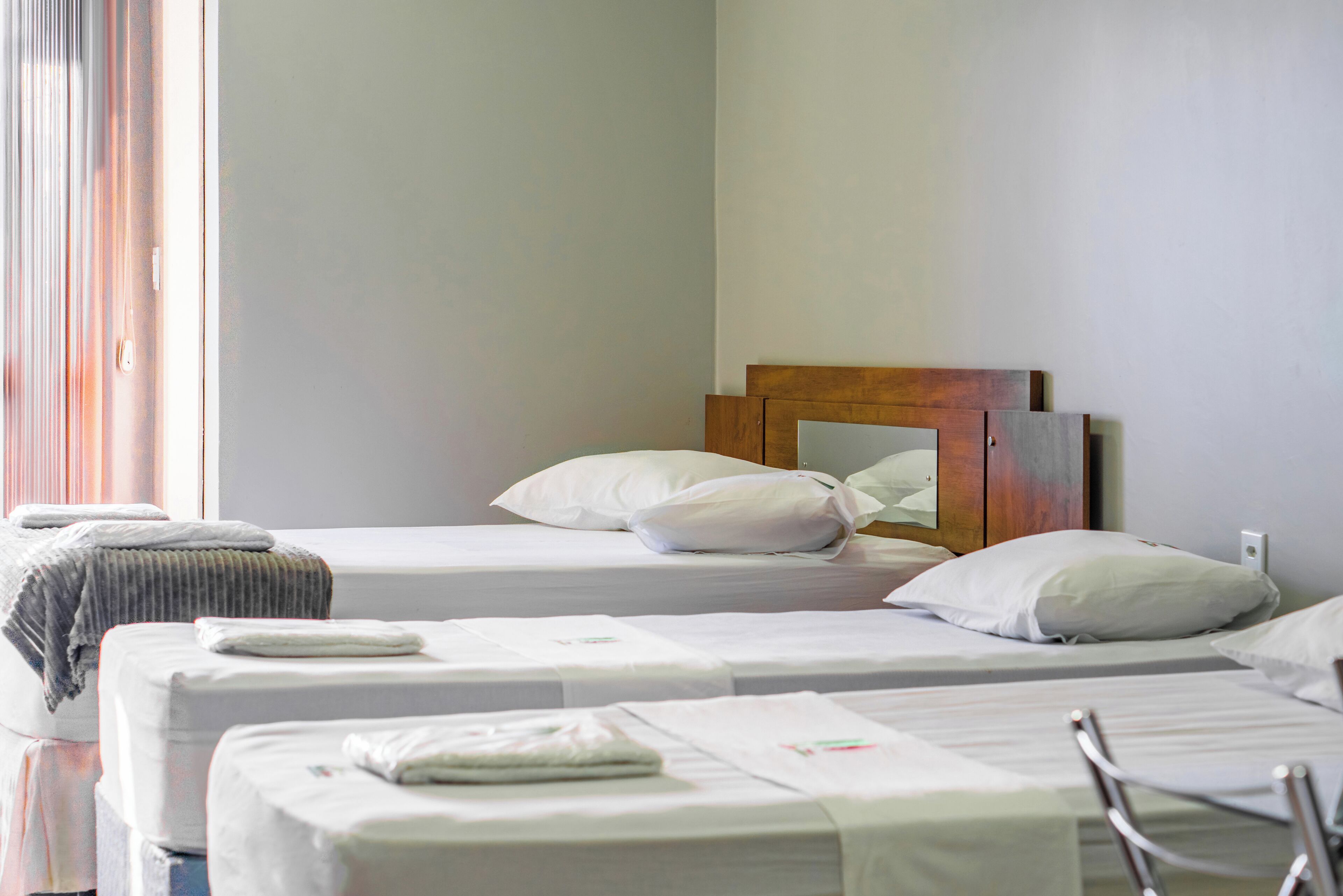 A hotel room with two single beds, a wooden headboard, white bedding, and a window with curtains.