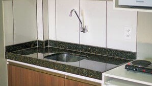 A kitchen with a granite countertop, stainless steel sink, and wooden cabinets. - Pinheiro Flat Hotel (Ibiapina)