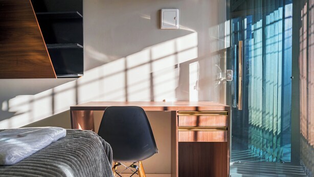 A modern bedroom with a wooden desk, a black chair, and a bed with a grey blanket. - Pinheiro Flat Hotel (Ibiapina)