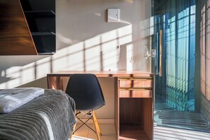 A modern bedroom with a wooden desk, a black chair, and a bed with a grey blanket. - Pinheiro Flat Hotel (Ibiapina)