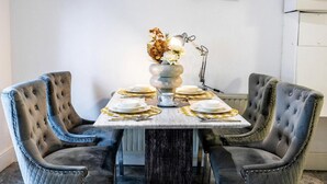 Una mesa de comedor con tapa de mármol blanco, rodeada por cuatro sillas con capitoné. Un jarrón con flores está sobre la mesa, y se ve una lámpara al fondo.