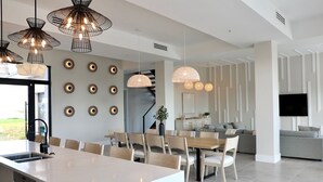 Een moderne keuken met een centraal eiland, een eethoek met stoelen, en een zithoek met een bank en televisie.