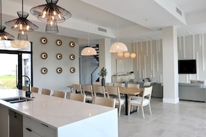 Una cocina moderna con una isla central, comedor con sillas y sala de estar con sofá y televisor.