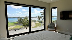 Een slaapkamer met een groot bed, een televisie en uitzicht op een strand en palmbomen.
