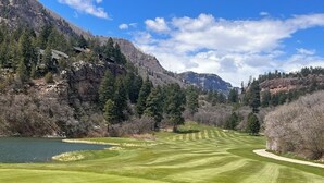 Een golfbaan met een meer, omringd door bergen en bomen.