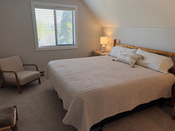 A bedroom with a large bed, a chair, a nightstand with a lamp, and a window with blinds. - Incredible Views, Large Deck, Wood Burning Fireplace! Havland Lake 3bed/3bath (Durango)