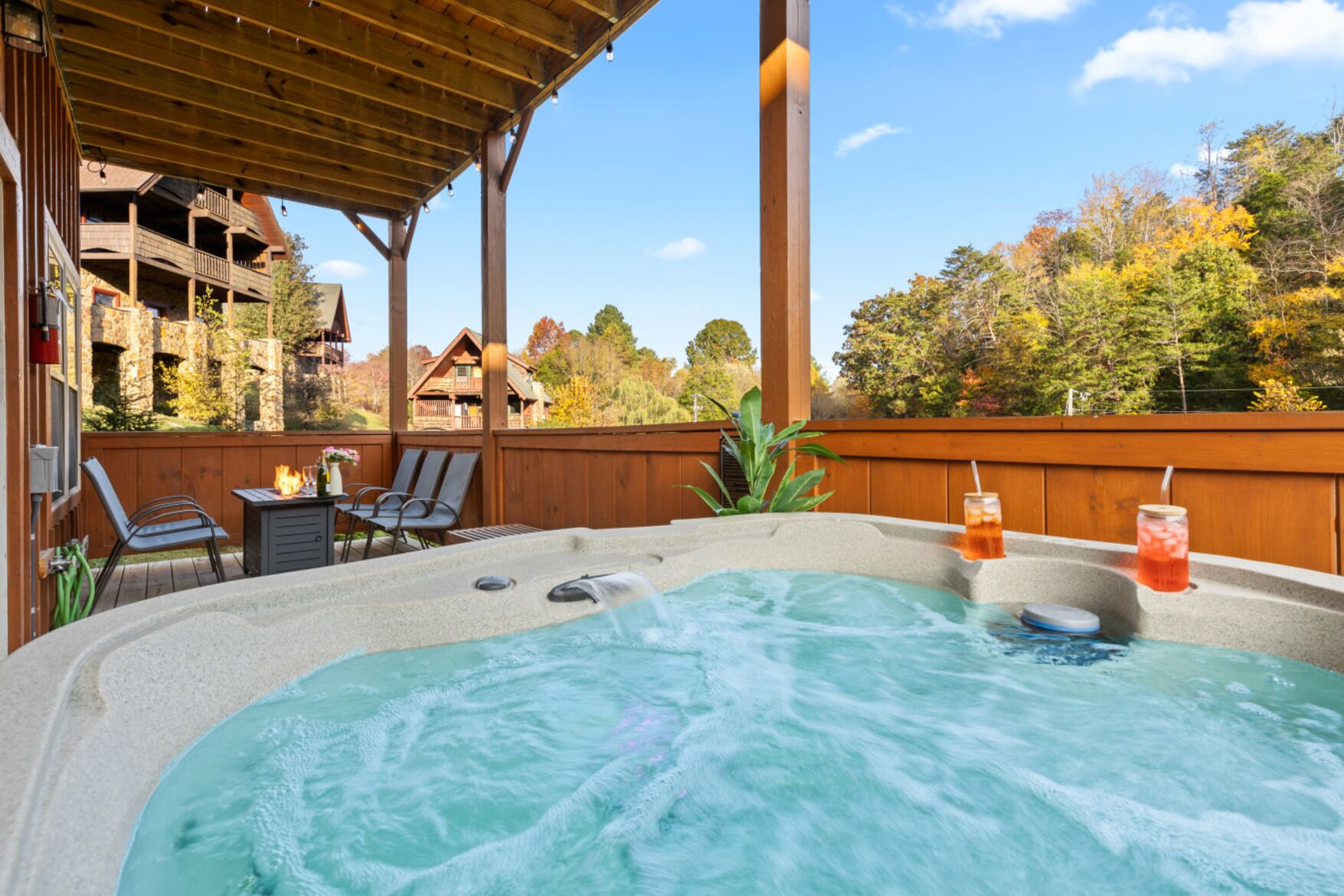 A hot tub with a wooden deck, lounge chairs, and a wooden fence.