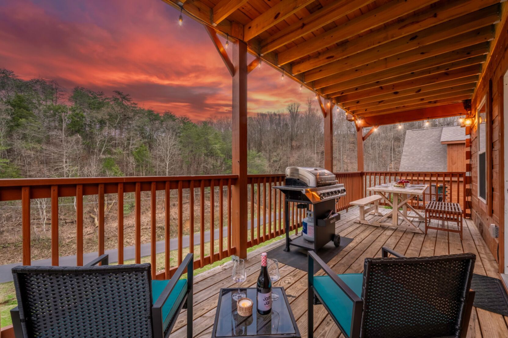 A covered outdoor deck with a barbecue, seating, and a scenic view of trees and hills.