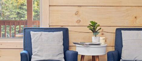 Two blue armchairs with striped pillows, a small white table with a plant, and a framed picture on a wooden wall.