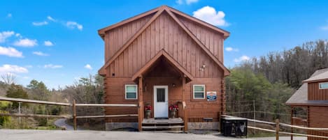 A wooden cabin with a front porch, a door, and a small sign on the side.